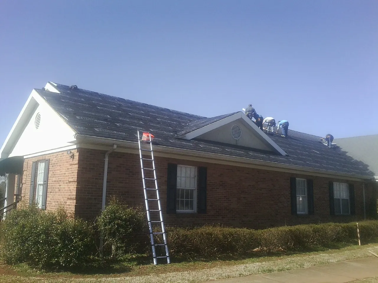 Crew tearing shingles off a brick ranch roof with a ladder set — Emergency Roof Repair work by our crew in Coalmont