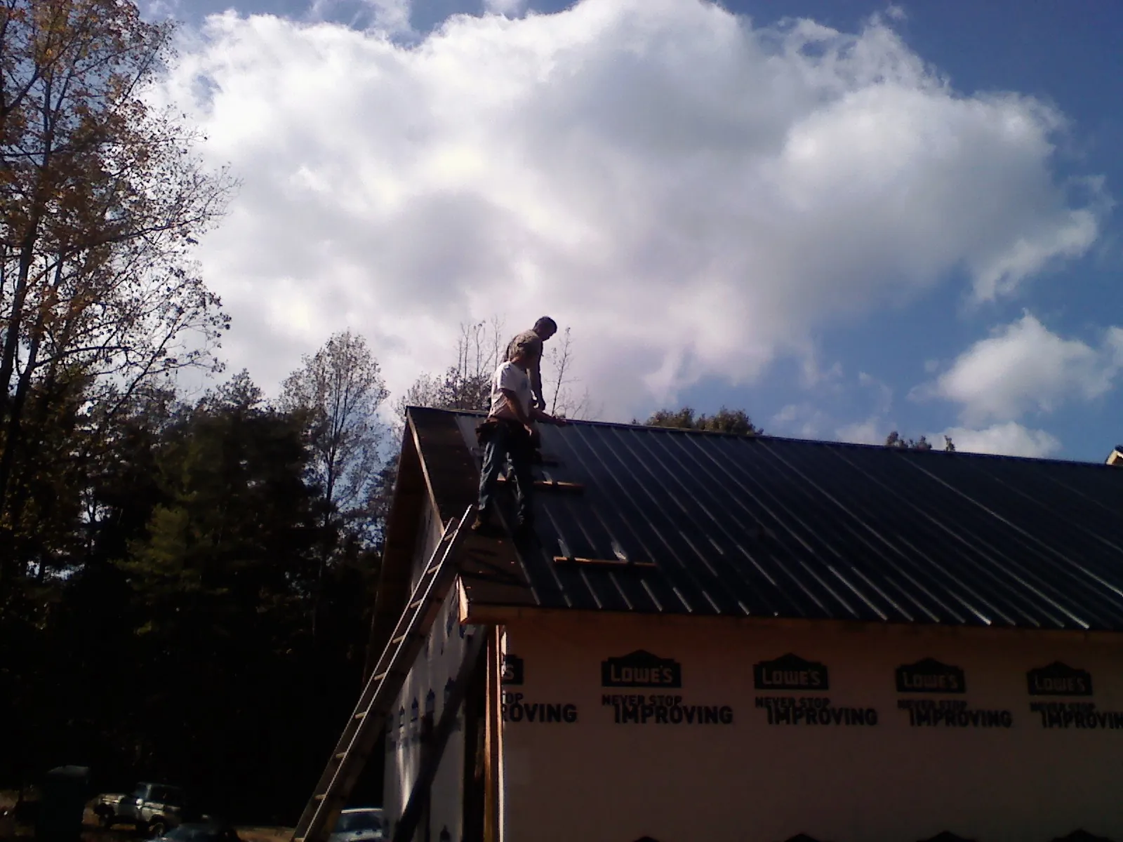 Roofer fastening dark metal panels high against a cloudy sky, from a Roof Inspection job in Coalmont