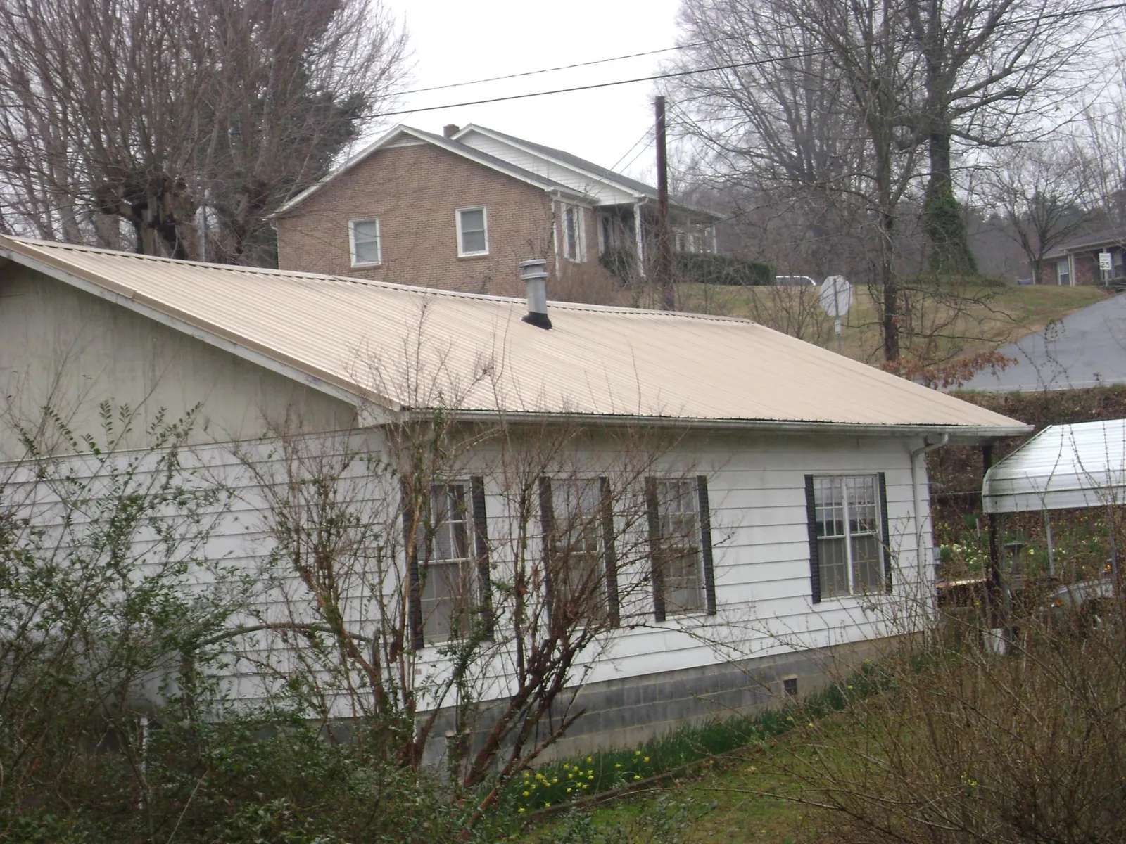 Tan metal roof on a white sided house set into a hillside — Commercial Roofing by Roofing Brothers in Coalmont